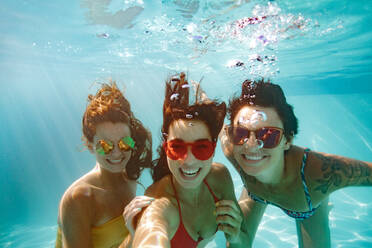Cheerful women friends swimming underwater in pool taking selfie. Underwater selfie of happy females in pool. - JLPSF25393