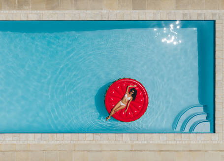 Luftaufnahme einer Frau, die auf einer aufblasbaren Matratze im Schwimmbad liegt. Entspannte Frau, die auf einer aufblasbaren Matratze im Schwimmbad schwimmt. - JLPSF25397