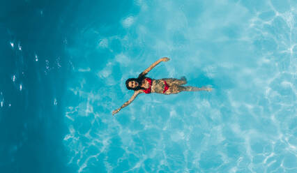 Luftaufnahme einer Frau beim Schwimmen im Pool eines Ferienortes. Ansicht von oben auf eine Frau, die das Schwimmen in einem Pool genießt. - JLPSF25402