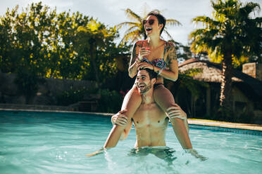 Gut aussehender junger Mann, der seine schöne Freundin auf der Schulter trägt und im Schwimmbad lacht. Junges Paar, das sich im Schwimmbad amüsiert. - JLPSF25407