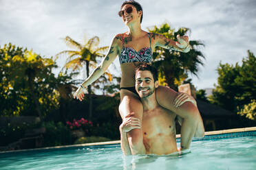 Mädchen sitzt auf den Schultern ihres Freundes im Schwimmbad. Paar hat Spaß im Schwimmbad an einem Sommertag. - JLPSF25408