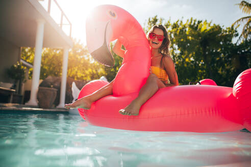 Junge Frau hat Spaß und lacht auf einer aufblasbaren Flamingo-Pool-Schwimmmatratze. Attraktive Frau an einem Sommertag im Pool. - JLPSF25411