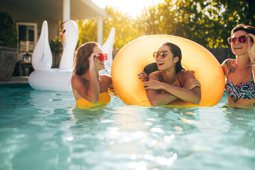 Glückliche junge Freundinnen im Schwimmbad mit aufblasbarem Ring. Lächelnde Frauen, die sich in einem Pool vergnügen. - JLPSF25412