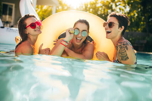 Drei Freundinnen genießen zusammen im Pool mit einem Schwimmring. Gruppe von Frauen lächelnd in einem Schwimmbad. - JLPSF25413
