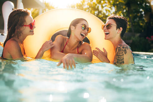 Fröhliche Frauen Freunde lachen und genießen im Schwimmbad mit aufblasbaren Ring. Frauen, die Spaß in Pool-Party. - JLPSF25414