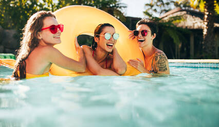 Gruppe von glücklichen jungen Freundinnen, die den Sommer am Pool genießen. Schöne lächelnde Frauen im Schwimmbad mit Sonnenbrille. - JLPSF25415