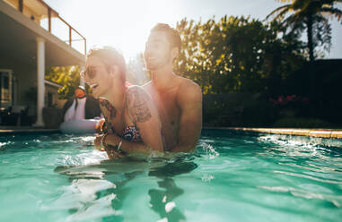 Smiling man and woman having fun in swimming pool. Couple enjoying themselves in pool on a summer day. - JLPSF25423