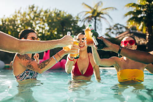 Fröhliche Freunde, die mit Bierflaschen in einem Schwimmbad feiern. Gruppe von Männern und Frauen im Schwimmbad, die mit Bier anstoßen. - JLPSF25424