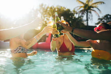 Friends toasting beer bottles in swimming pool party. Group of men and women in swimming pool having beers. - JLPSF25425