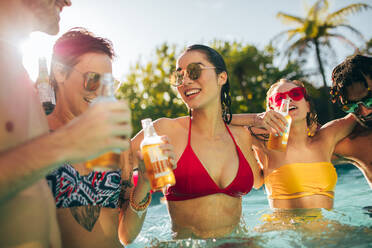 Fröhliche Gruppe von Freunden, die sich auf einer Poolparty amüsieren. Eine Gruppe von Männern und Frauen, die sich gemeinsam im Schwimmbad mit Getränken vergnügen. - JLPSF25432