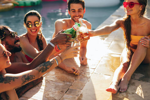 Freunde trinken Bier auf einer Pool-Party. Mehrrassige Männer und Frauen, die auf einer Pool-Party Getränke genießen und darauf anstoßen. - JLPSF25436