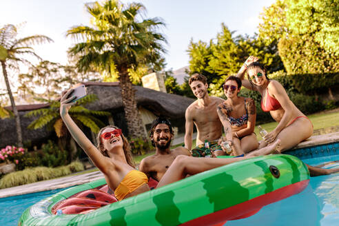 Hübsches Mädchen, das ein Selfie mit Freunden in einem Swimmingpool macht. Freunde, die Spaß haben und sich in einem Resort im Urlaub entspannen. Poolparty-Selfie. - JLPSF25451