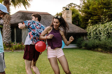 Frau versucht, einen Ballon mit ihren Hüften auf dem Rücken eines Mannes zum Platzen zu bringen. Freunde spielen Ballonzerstecherspiele auf einer Party im Freien. - JLPSF25453