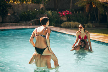 Frauen sitzen auf den Schultern ihres Freundes im Schwimmbad und haben Spaß. - JLPSF25483