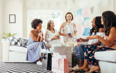 Glückliche schwangere Frau mit weiblichen Freunden, die Getränke bei einer Babyparty halten. Gruppe von multiethnischen Frauen, die bei einer Babyparty mit Geschenken sitzen. - JLPSF25486