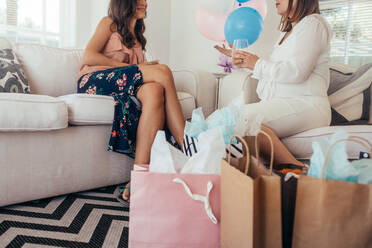 Baby-Dusche Geschenke mit Frauen auf dem Sofa im Hintergrund und im Gespräch. Schwangere Frau im Gespräch mit weiblichen Freund auf Baby-Dusche. - JLPSF25502