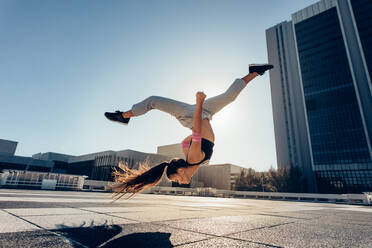 Young sportswoman performing a front flip outdoors in city. Female athlete practicing tricking against an urban background. - JLPSF25533