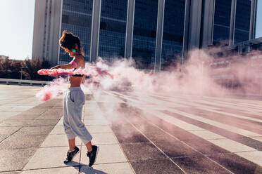 Woman holding colorful smoke grenade outdoors in city. Urban sportswoman with smoke sticks. - JLPSF25534