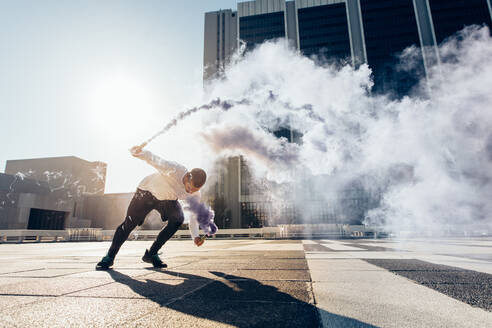 Sportlicher Mann, der Parkour und freies Laufen übt, indem er einen Salto mit einer Rauchgranate macht. - JLPSF25536