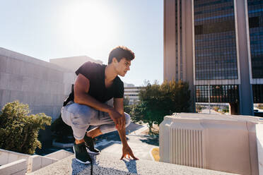 Young sportsman squatting outdoors before demonstrating parkour and free running techniques. Fit young man getting ready to practice freerunning in city. - JLPSF25537