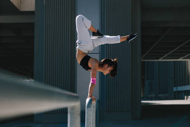 Sportlerin, die einen Handstand auf einem Geländer im Freien macht. Flexible weibliche Athletin, die Extremsportarten in einem städtischen Raum betreibt. - JLPSF25542