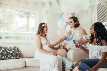 Lächelnde schwangere Frau mit Freundinnen bei einer Babyparty. Gruppe von Freundinnen trifft sich zu einer Babyparty zu Hause. - JLPSF25553