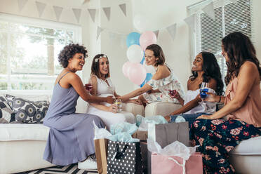 Eine Gruppe multiethnischer Freundinnen besucht eine Babyparty zu Hause. Freunde berühren den Babybauch einer schwangeren Frau. - JLPSF25554