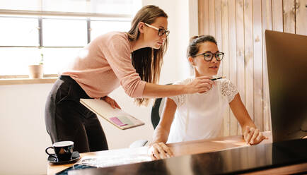 Kreative Geschäftsfrauen, die zusammen an einem Desktop-Computer im Büro arbeiten. Zwei weibliche Mitarbeiter arbeiten und schauen auf den Computerbildschirm. - JLPSF25557