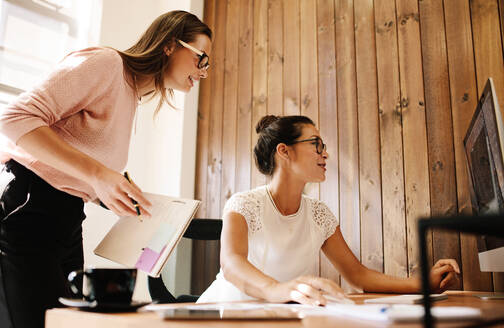 Geschäftsfrauen arbeiten gemeinsam an einem Projekt in einem modernen Startup-Büro. Zwei Kolleginnen schauen auf einen Computerbildschirm. - JLPSF25558