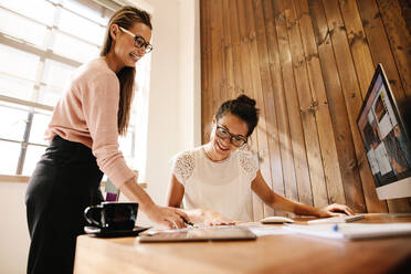 Lächelnde kreative Geschäftsfrauen am Bürotisch. Zwei weibliche Mitarbeiter arbeiten zusammen. - JLPSF25562