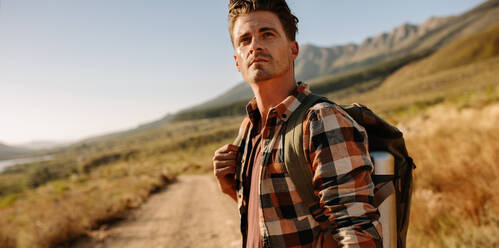 Handsome young guy with backpack walking down the mountain trail. Male  hiking in nature on a summer day. stock photo