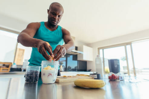 Man preparing milk shake in kitchen. Athletic man adding fruits to jar of milk. - JLPSF25592