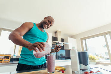 Mann bereitet Milchshake in der Küche zu. Lächelnder Mann gießt Milchshake in ein Glas zum Trinken. - JLPSF25593
