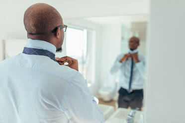 Ein Mann, der sich eine Krawatte umbindet, schaut in einen Spiegel. Rückenansicht eines Geschäftsmannes, der eine Krawatte trägt. - JLPSF25597