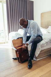 Businessman checking his bag sitting on bed. Man getting ready to go to office. - JLPSF25598