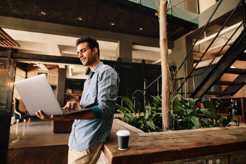 Shot of young creative man in company lounge working on laptop. Businessman in modern office using laptop. - JLPSF25605