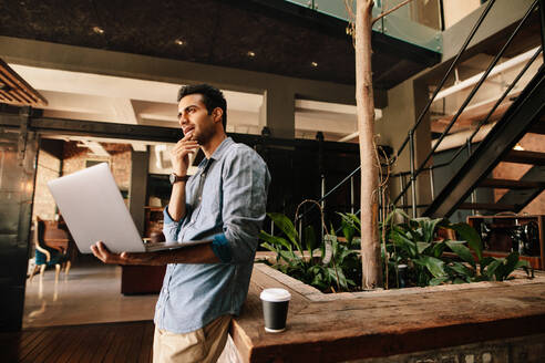 Aufnahme eines jungen Geschäftsmannes, der in der Pause mit seinem Laptop nachdenkt. Geschäftsmann in einem modernen Büro mit Laptop. - JLPSF25606