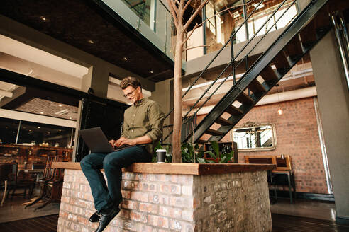 Young man sitting in office cafeteria working on laptop. Creative executive using laptop computer during coffee break. - JLPSF25608