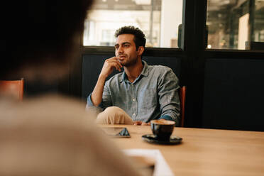 Gut aussehender junger Mann, der an einem Tisch im Konferenzraum sitzt und einem Kollegen zuhört. Mann während einer Geschäftsbesprechung. - JLPSF25615