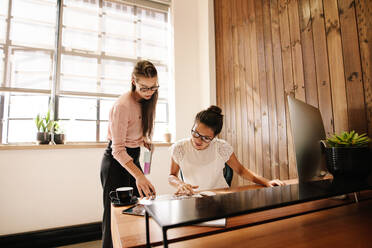 Zwei Geschäftsfrauen lesen Dokumente auf dem Schreibtisch, Kollegen arbeiten in einem modernen Büro zusammen. - JLPSF25635