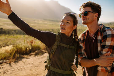 Junges Paar auf einem Wanderausflug, wobei die Frau ihrem Freund die Aussicht zeigt. Junges Paar auf einem Feldweg. - JLPSF25640