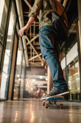 Rückansicht eines Mannes, der im Büroflur Skateboard fährt. Junger Geschäftsmann, der durch sein Startup-Büro skatet. - JLPSF25649