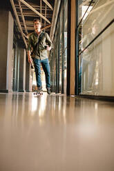 Full length shot of young man skateboarding in office. Casual businessman skating through office corridor. - JLPSF25650