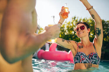 Schöne junge Frau im Bikini tanzt mit Bier in der Hand auf einer Poolparty und feiert mit Freunden an einem Sommertag. - JLPSF25657