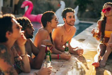 Eine Gruppe von Männern und Frauen unterhält sich und trinkt auf einer Poolparty. Freunde genießen einen Sommertag am Pool. - JLPSF25659