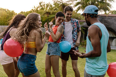 Eine Gruppe von Männern und Frauen spielt Ballonplatzen auf einer Party. Freunde genießen es, Spiele auf einer Party im Freien zu spielen. - JLPSF25660