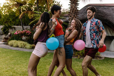 Eine Gruppe von Freunden spielt auf einer Party ein Luftballonwettrennen, bei dem Männer und Frauen versuchen, den Ballon des jeweils anderen zum Platzen zu bringen. - JLPSF25661