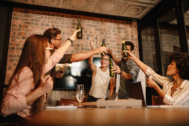 Eine Gruppe erfolgreicher junger Geschäftsleute, die bei einem Bier feiern. Eine bunt gemischte Gruppe von Menschen, die bei einem erfolgreichen Geschäftsabschluss etwas trinken. - JLPSF25667