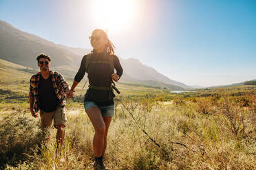 Glückliches junges Paar beim gemeinsamen Wandern an einem Sommertag. Junge Frau mit ihrem Freund beim Spaziergang durch die Landschaft. - JLPSF25693