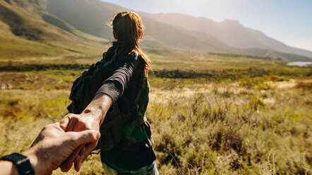 Junge Frau hält die Hand ihres Freundes, während sie durch extremes Gelände wandert. Paar auf einer Wanderung in der Natur. Blickwinkel. - JLPSF25698